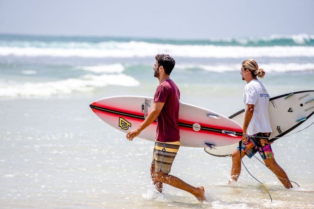 Two surfers carrying boards on a sunny day at Dambulla Beach, Sri Lanka.