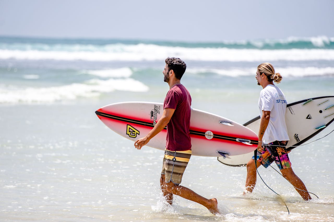Two surfers carrying boards on a sunny day at Dambulla Beach, Sri Lanka.